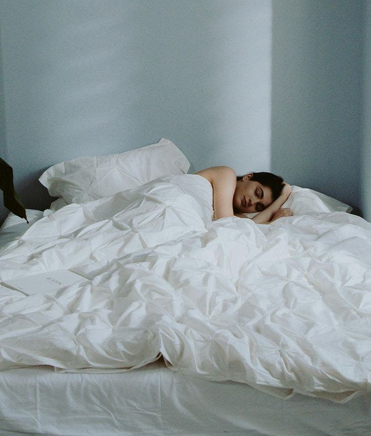 woman laying in bed with rumpled white duvet