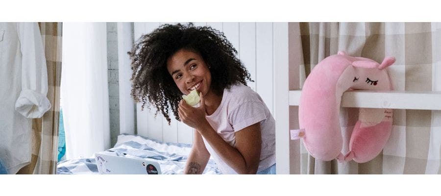 Young woman eating an apple in bed and working on a laptop