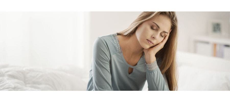 Woman sitting on her mattress with her head in her hands