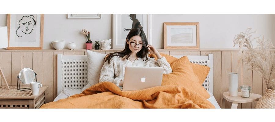 Young woman sitting up in bed and researching fiberglass in mattresses