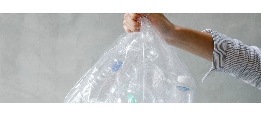 Person holding a clear plastic bag full of recyclable plastic bottles