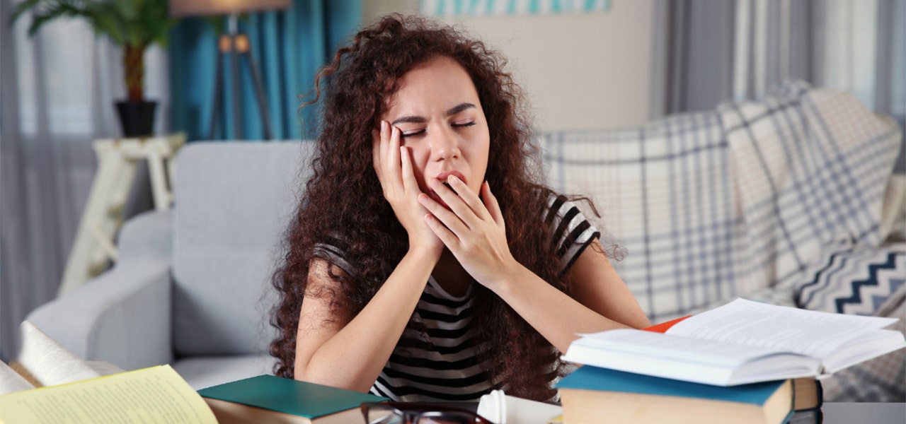 College student yawning in front of a stack of text books