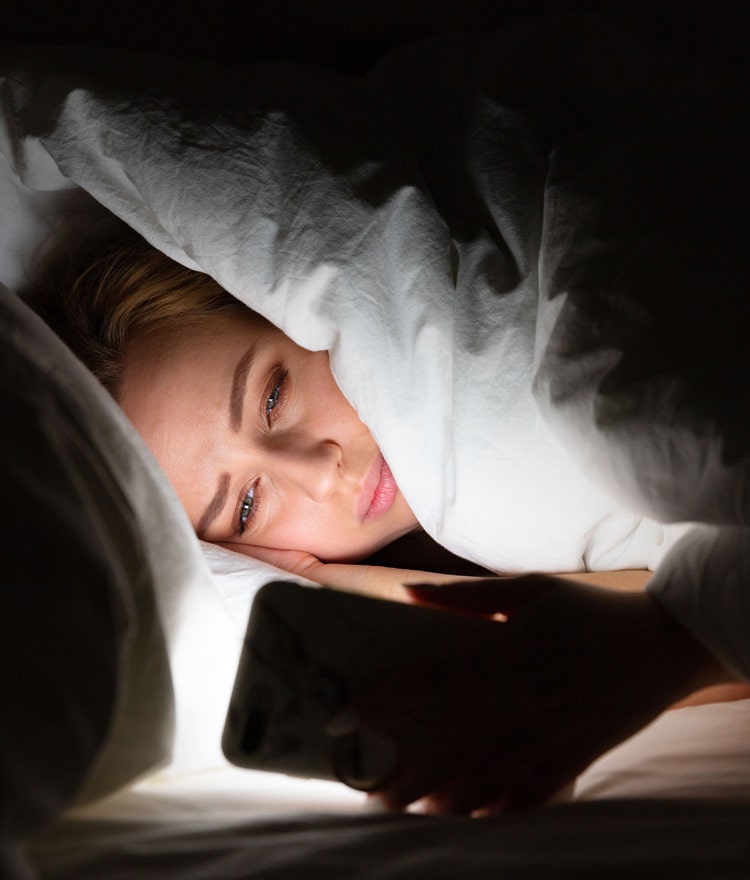 Woman looking at her phone while inder the covers in a dark room
