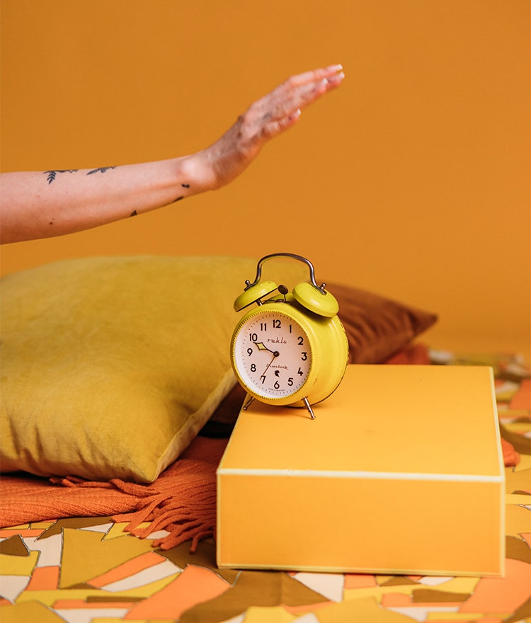 Woman's hand turning off a bright yellow alarm clock