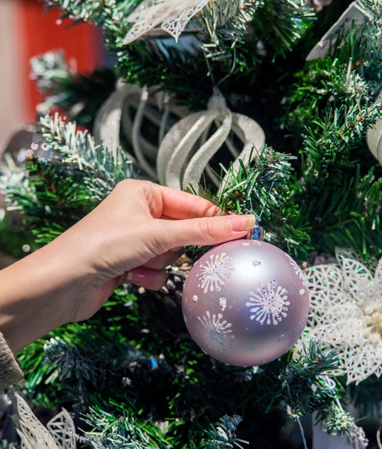 Woman hanging a silver ornament on a holiday tree