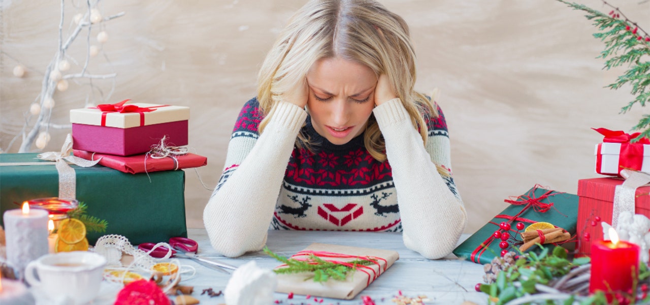 Woman wearing a holiday sweater and wrapping gifts but looking very stressed out