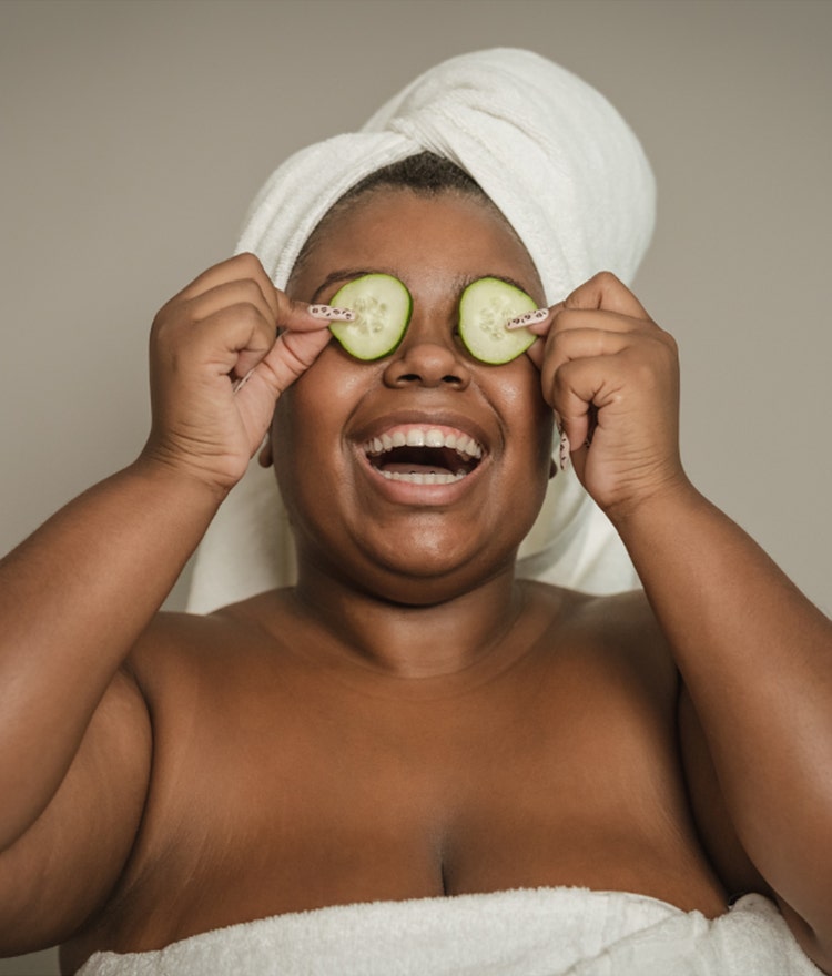 Woman with a towel on her head and cucumbers over her eyes