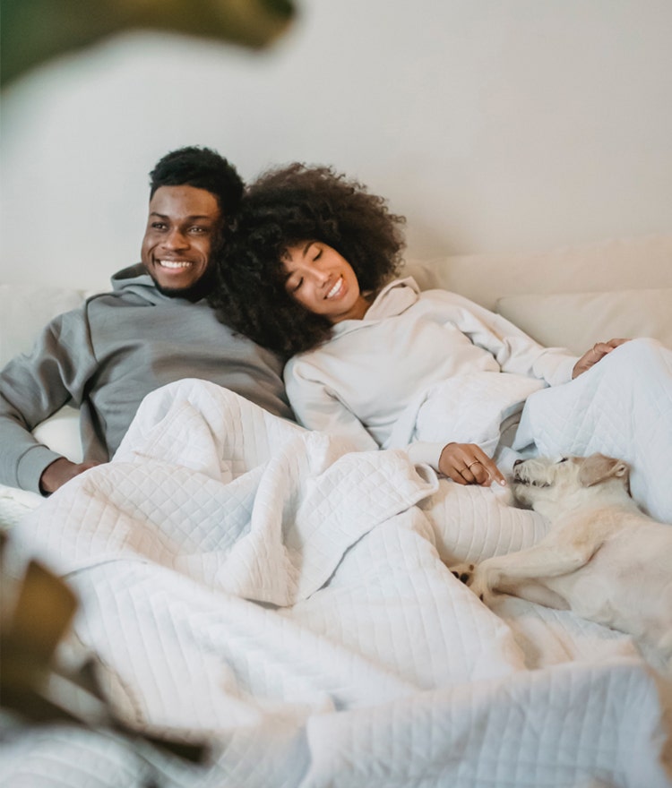 Happy, well-rested couple relaxing in bed with their dog