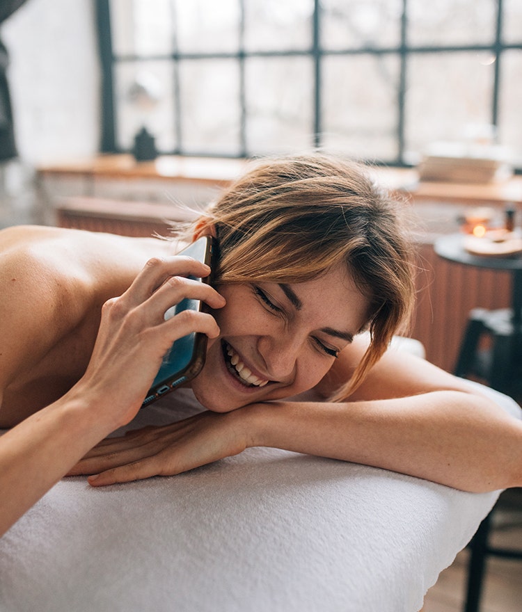 Young woman lying in bed and laughing on a phone call