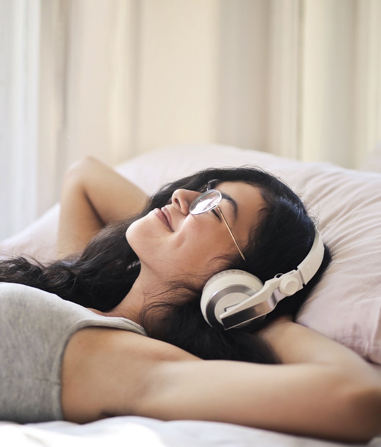 Woman relaxing in bed and listening to music via headphones