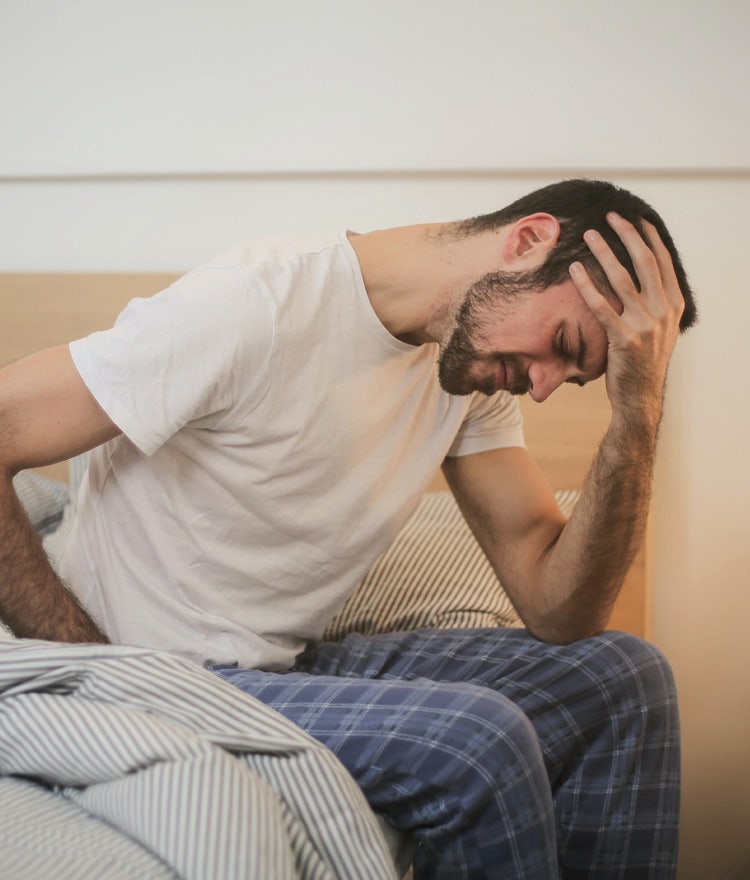 Tired man sitting on the edge of his bed, looking stressed out