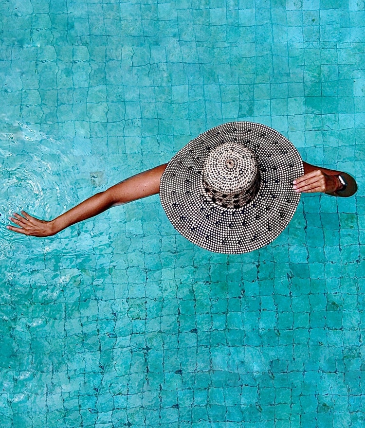 Woman with a sunhat wading in a swimming pool