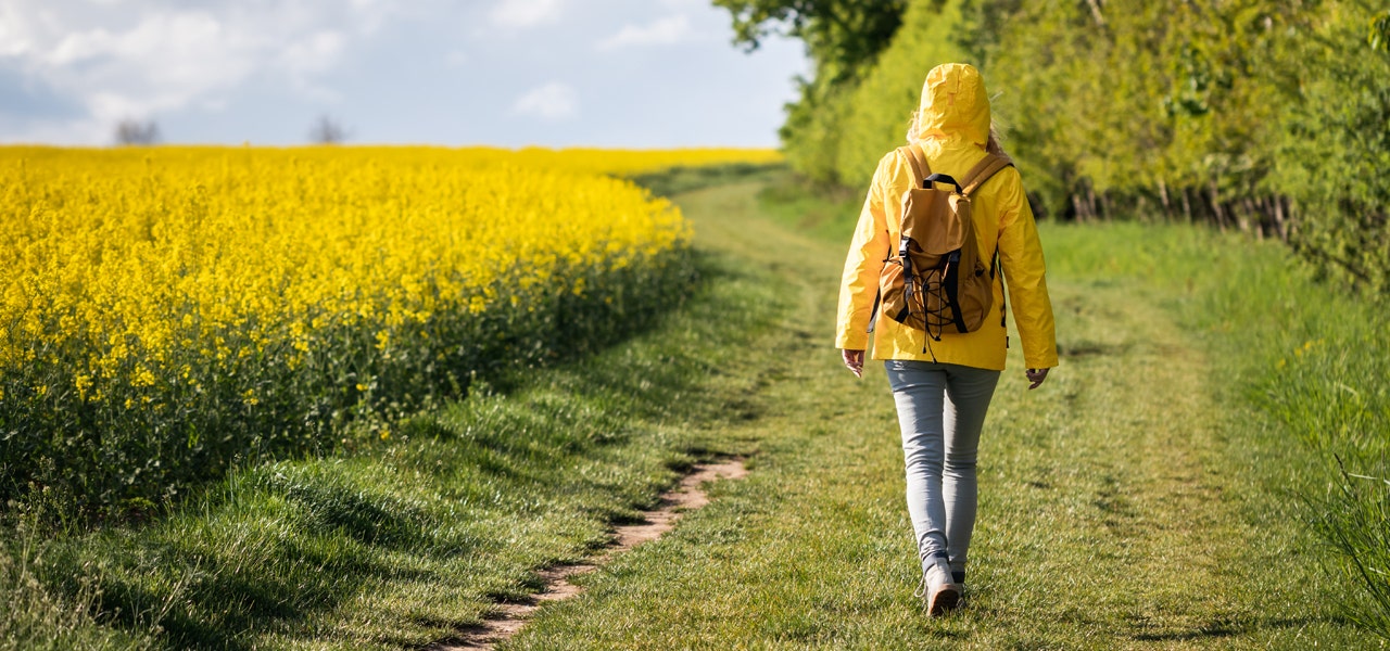 Woman in a yellow jacket walking near a field of yellow flowers