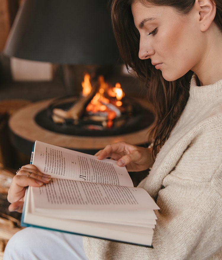 Woman relaxing with a book by a cozy fire