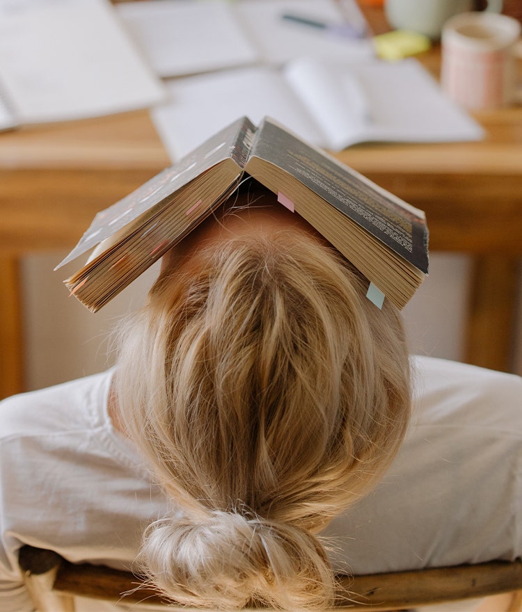 Tired college student balancing a book on their face