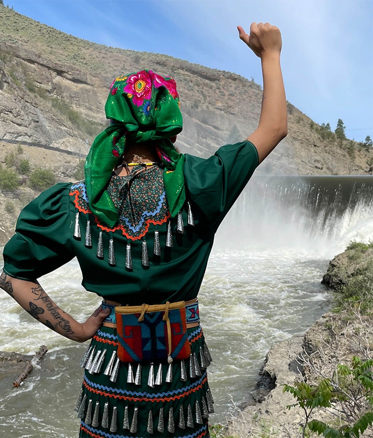 Woman facing a majestic waterfall and raising a fist in celebration