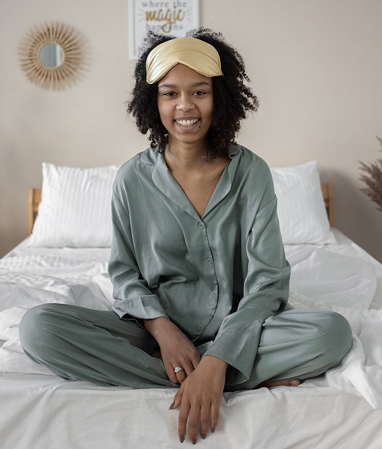 Smiling woman relaxing on her bed in PJs with a sleep mask pulled up