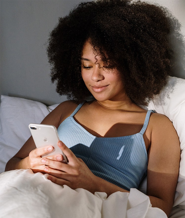 Woman sitting up in bed researching on her phone