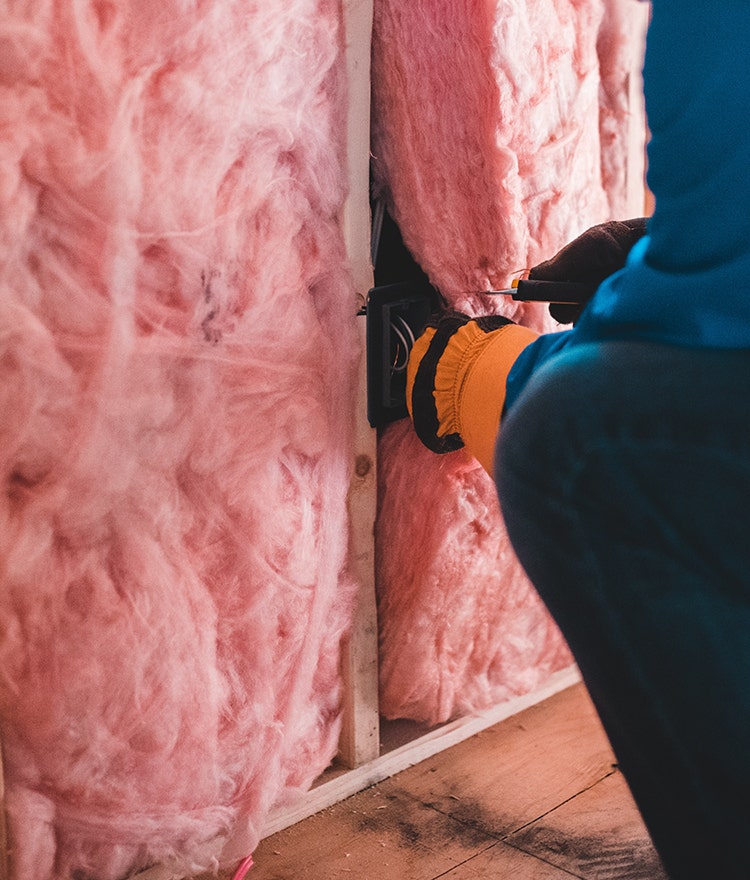 A person installing pink fiberglass home insulation