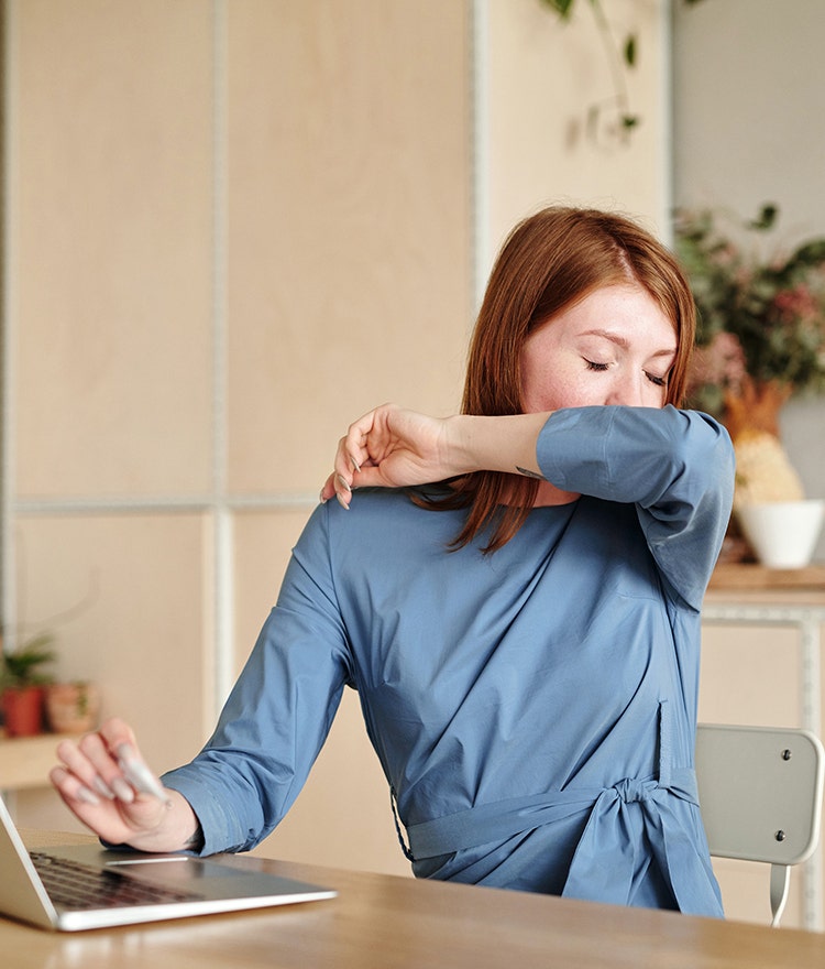 Woman working at a laptop and coughing into her arm