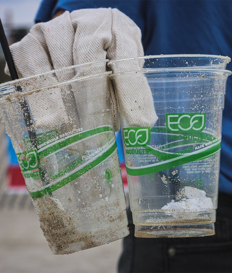 Someone picking up dirty plastic cups 'labeled "eco" from the beach