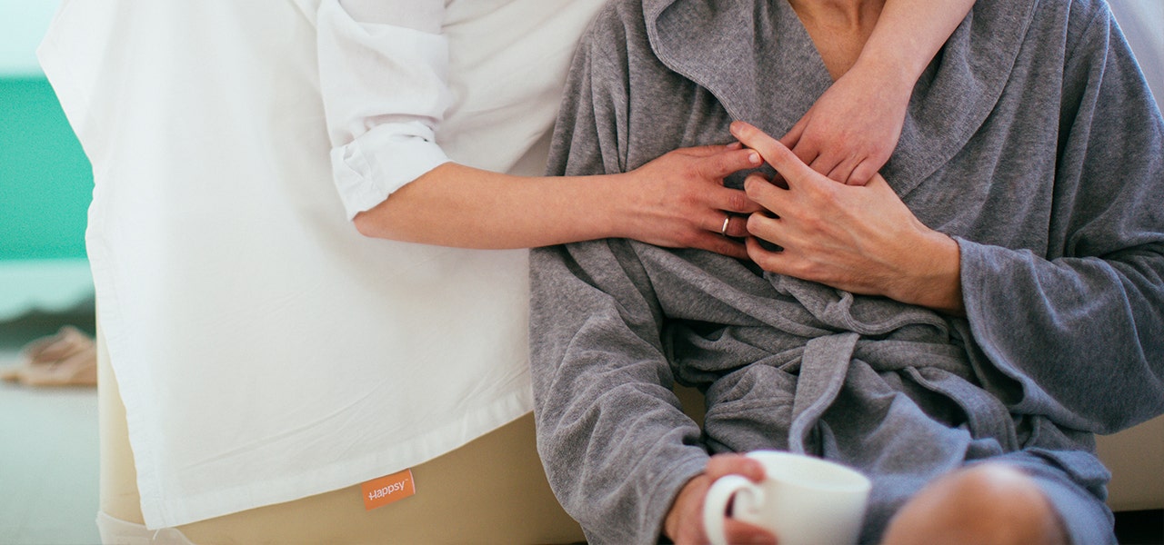 Couple leaning against their bed with a Happsy organic sheet draped over the side