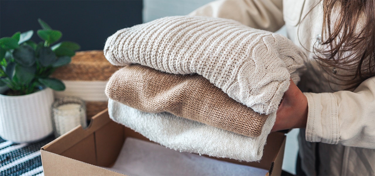a pile of folded sweaters being placed in a cardboard box